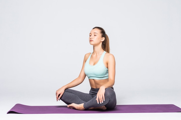 Portret całkiem młoda kobieta robi medytację ćwiczenia jogi na macie na białym tle
