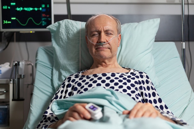 Bezpłatne zdjęcie portret chorego starszego pacjenta odpoczywającego w łóżku szpitalnym, oddychającego z pomocą maski tlenowej z powodu infekcji płuc, z oksymetrem przymocowanym do palca