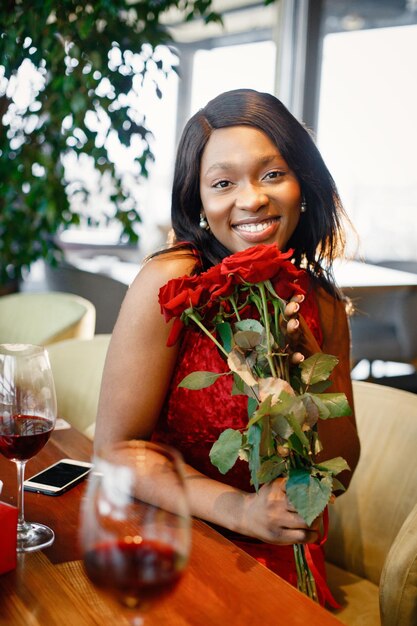 Portret czarnej kobiety trzymającej bukiet czerwonych róż, siedząc w restauracji