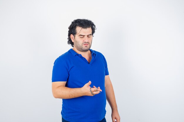 Portret dojrzałego mężczyzny trzymającego łańcuch zawinięty ręcznie w niebieską koszulkę i patrząc zamyślony widok z przodu