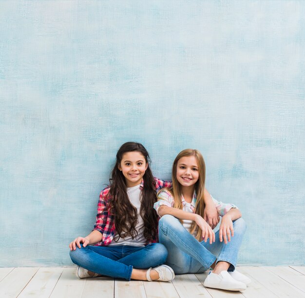 Portret dwa uśmiechniętej dziewczyny siedzi wpólnie przeciw malującej błękitnej ścianie