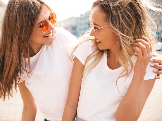 Portret dwóch młodych pięknych blond uśmiechnięte dziewczyny hipster w modne letnie białe ubrania t-shirt. .