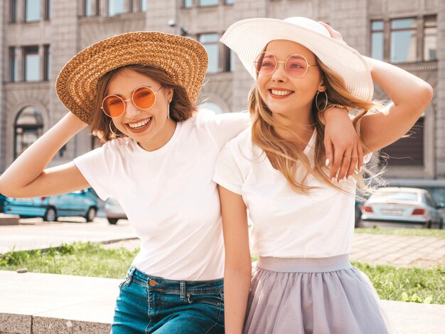 Portret dwóch młodych pięknych blond uśmiechnięte dziewczyny hipster w modne letnie białe ubrania t-shirt. .