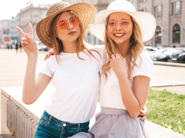 Portret dwóch młodych pięknych blond uśmiechnięte dziewczyny hipster w modne letnie białe ubrania t-shirt. .