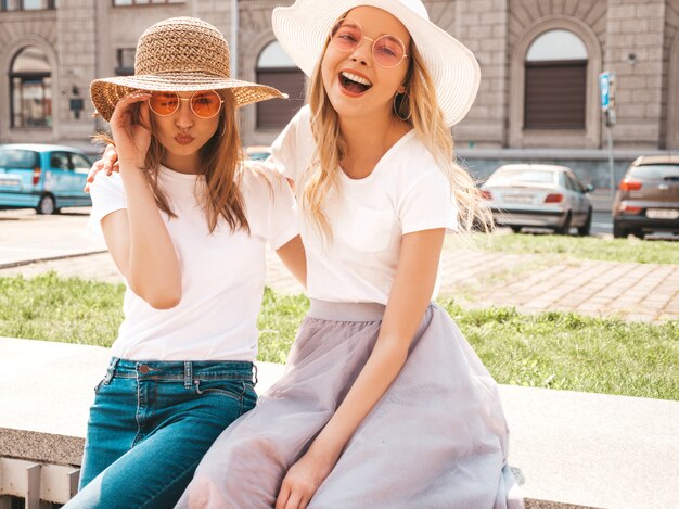 Portret dwóch młodych pięknych blond uśmiechnięte dziewczyny hipster w modne letnie białe ubrania t-shirt. .