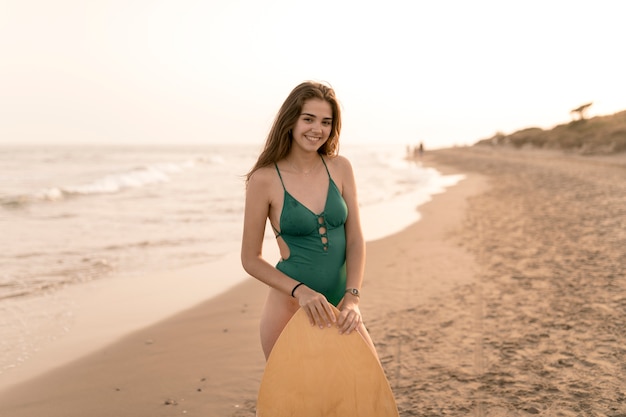 Portret dziewczyna w zielonej bikini pozyci blisko piaskowatej plaży z ciała deską