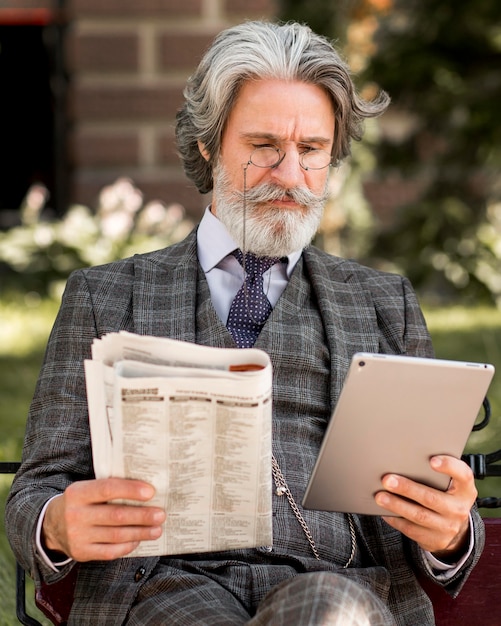 Bezpłatne zdjęcie portret elegancki dojrzały mężczyzna trzymając tabletkę i gazetę