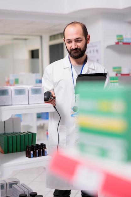 Bezpłatne zdjęcie portret farmaceuty sprawdzającego listę leków na tablecie podczas skanowania opakowań tabletek za pomocą skanera sklepowego w aptece. pracownik apteki jest odpowiedzialny za uporządkowanie i oznakowanie leków