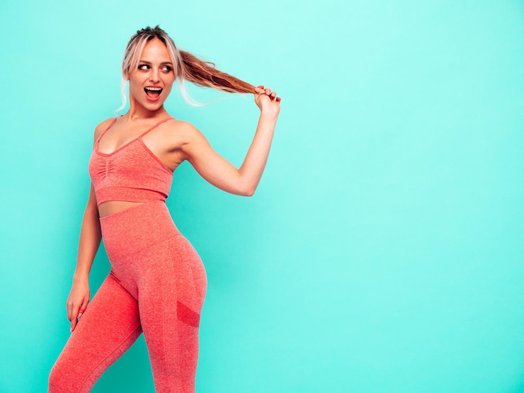 Bezpłatny plik Zdjęcie portret fitness uśmiechnięta kobieta w różowej odzieży sportowej młody piękny model z idealnym ciałemkobieta pozuje w pobliżu niebieskiej ściany w studiowesoły i szczęśliwy trzymając ogon włosów
