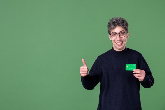 Portret genialnego mężczyzny trzymającego zieloną kartę kredytową w studio strzał zielona ściana