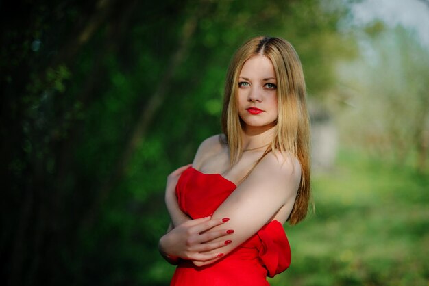 Portret jasnowłosej dziewczyny na czerwonej sukience w tle wiosennego ogrodu