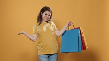 Bezpłatne zdjęcie portret kobiety dumnej z zakupu pokazujący emocje związane z kupowaniem produktów w studio. uśmiechnięta osoba trzymająca torby na zakupy czuje się zachwycona i zadowolona z zakupu na żółtym tle.