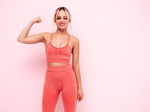 Portret kobiety fitness w różowej odzieży sportowej Młody piękny model z idealnym ciałemKobieta pozuje blisko ściany w studioWesoły i szczęśliwy Rozciąganie się przed treningiem