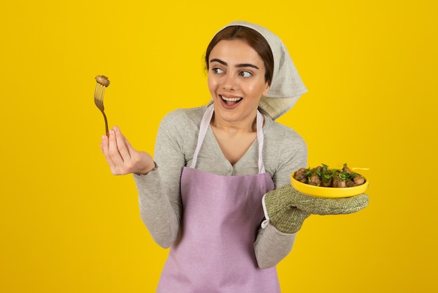 Portret kobiety kucharz w fioletowy fartuch jedzenie smażonych grzybów.