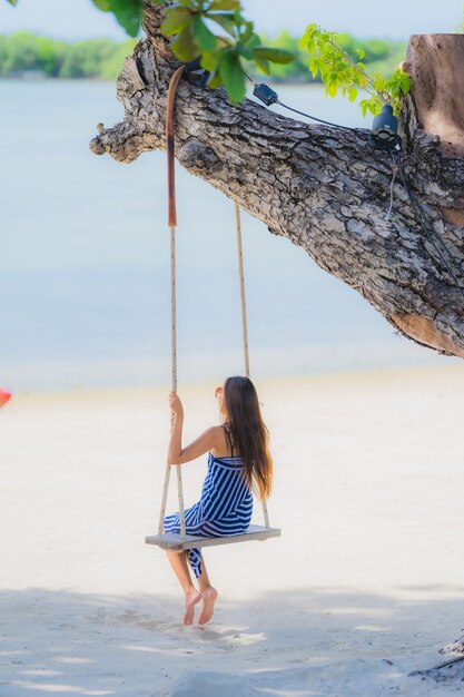 Portret kobiety młody azjatykci obsiadanie na huśtawkowej arkanie i morzu wokoło plażowego dennego oceanu kokosowego drzewka palmowego