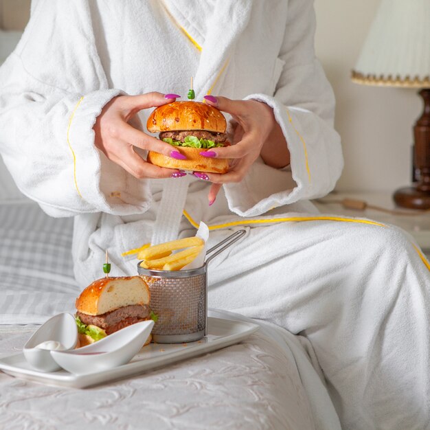 Portret kobiety o posiłek, jedzenie hamburgera w szlafroku