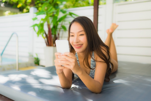 Portret kobiety piękny młody azjatykci uśmiech szczęśliwy relaksuje z telefonem komórkowym wokoło pływackiego basenu