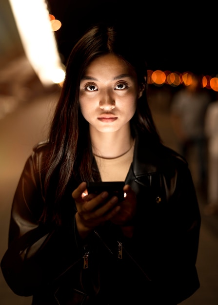 Portret kobiety przy użyciu smartfona w nocy w światłach miasta