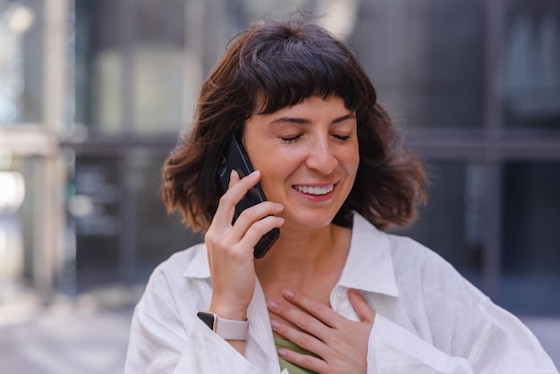 Portret kobiety uśmiechającej się z zamkniętymi oczami, rozmawiającej na telefonie komórkowym