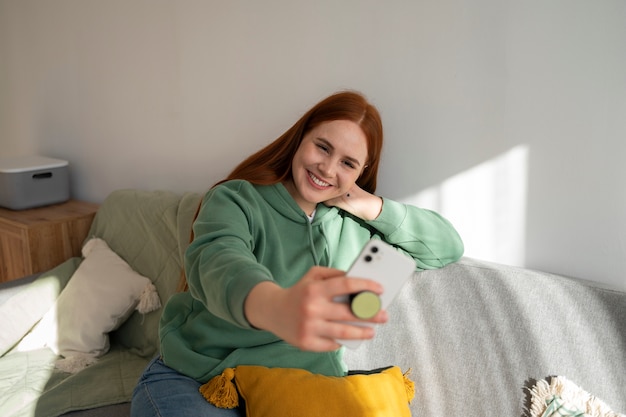 Portret kobiety używającej smartfona w domu na kanapie, trzymając ją z gniazda pop