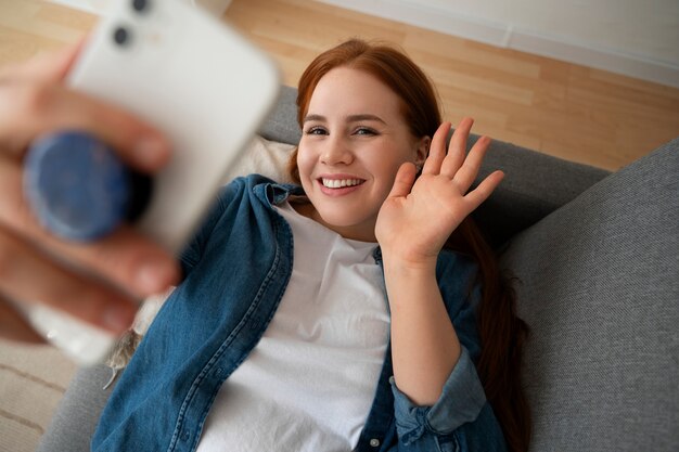 Portret kobiety używającej smartfona w domu na kanapie, trzymając ją z gniazda pop