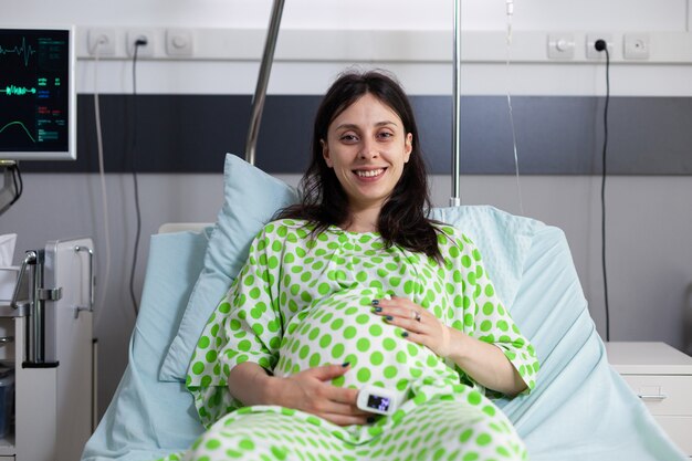 Portret kobiety w ciąży siedzącej w łóżku na oddziale szpitalnym
