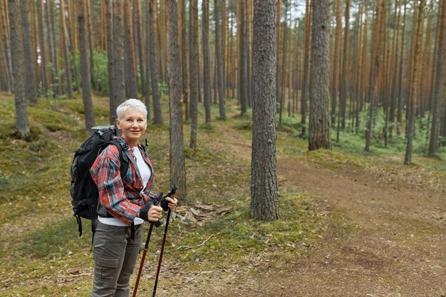 Portret kobiety w średnim wieku w odzieży sportowej stojącej na szlaku w parku narodowym przy użyciu kijów do nordic walking