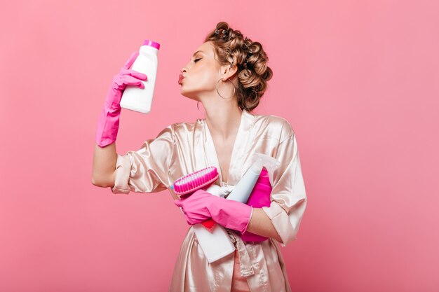 Portret kobiety w szlafroku, szczęśliwie pozowanie na różowej ścianie z detergentami