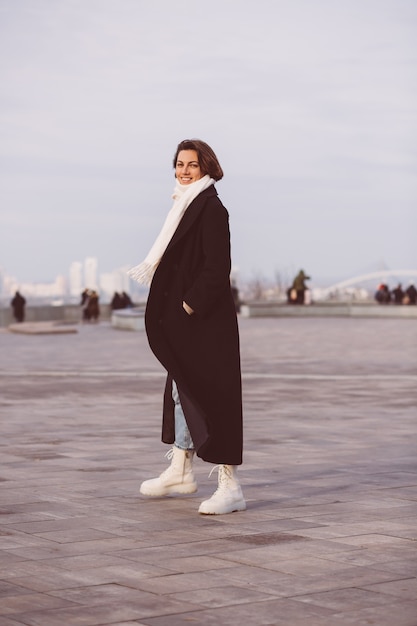 Portret kobiety w zimowy czarny płaszcz i biały szalik na placu miejskim.