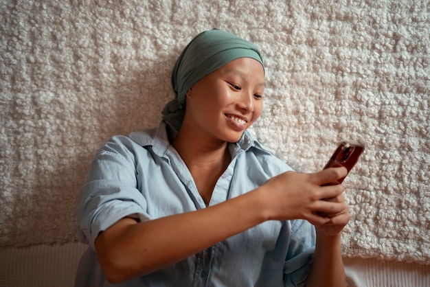 Portret kobiety z rakiem używającej smartfona w domu