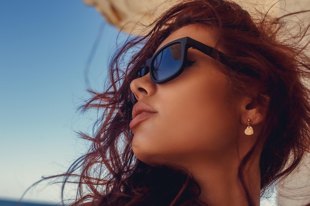 Portret kobiety z rudymi włosami w okularach przeciwsłonecznych.