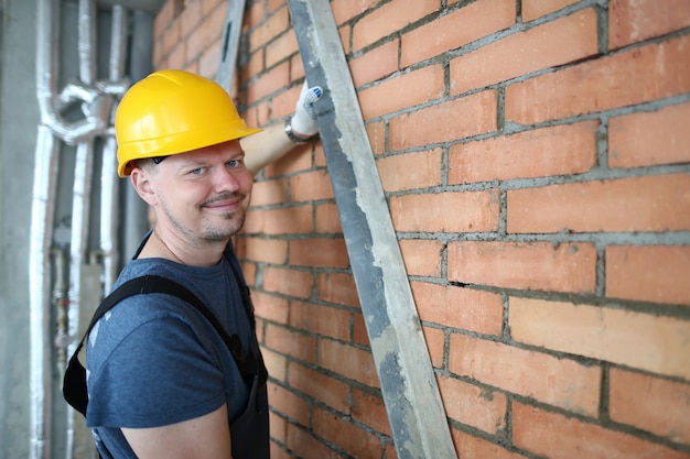 Portret konstruktora sprawiający, że ściana z cegieł jest gładka w celu tynkowania ściany z cegieł. uśmiechnięty mistrz budowlany w stroju ochronnym, aby zapobiec urazom. koncepcja budynku