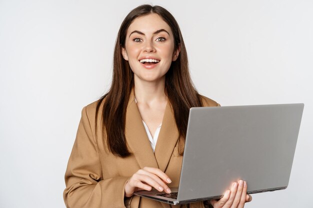 Portret korporacyjnej kobiety pracującej z laptopem uśmiecha się i wygląda asertywnie na białym tle