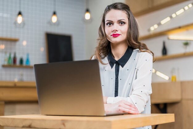 Portret ładna kobieta siedzi przed laptopem na drewnianym stole
