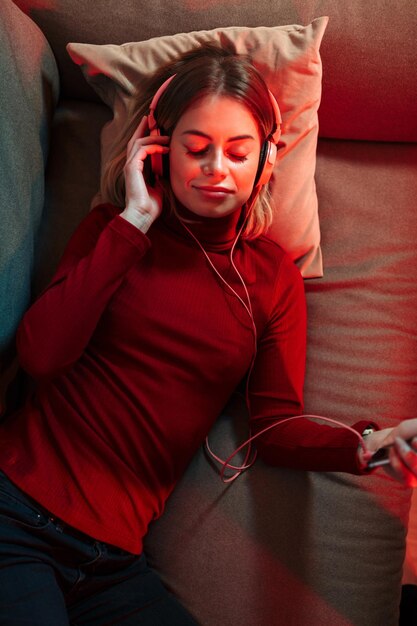 Portret ładnej damy w słuchawkach leżącej na kanapie i sennie słuchającej muzyki w domu