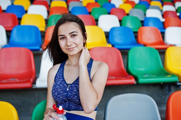 Portret ładnej kobiety w sportowej siedzącej i pitnej wodzie na stadionie