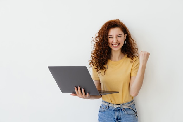 Portret ładnej młodej kobiety świętującej sukces na laptopie na białym tle