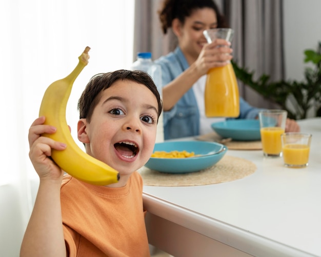 Portret ładny mały chłopiec bawi się bananem przy stole śniadaniowym