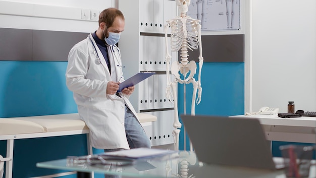 Bezpłatne zdjęcie portret lekarza pierwszego kontaktu w białym fartuchu i stetoskop uśmiechający się przed kamerą. mężczyzna lekarz posiadający wiedzę medyczną i przygotowujący się do wizyty kontrolnej.