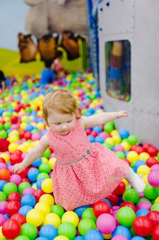 Portret mała śliczna dziewczynka księżniczka niemowlę 1-2 lata stojące i bawiące się balonami, kolorowe kulki na placu zabaw, basen z piłeczkami, suchy basen na przyjęcie urodzinowe. koncepcja obchodów pierwszego roku.