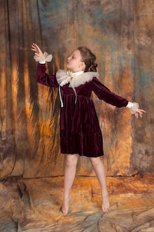 Portret małej księżniczki w bordowej klasycznej sukience z falbanką pozuje na vintage tle dziewczyna z idealnie lśniącymi długimi włosami styl retro i modny aby zamknąć zdjęcie studyjne