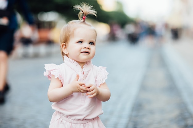 Portret małej, słodkiej, pięknej dziewczyny spaceruje po mieście w różowej sukience.