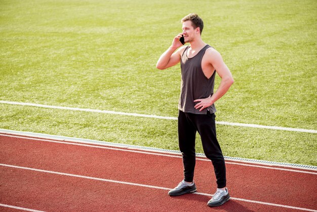 Portret męska atleta stoi na biegowym śladzie opowiada na mądrze telefonie