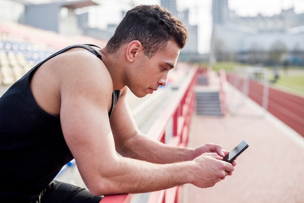 Portret męska atleta używa telefon komórkowego przy stadium