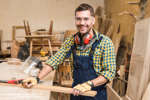 Portret męski cieśla trzyma drewnianą deskę na workbench w warsztacie