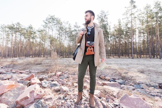 Portret męski wycieczkowicz trzyma rodzajową mapę w lesie patrzeje daleko od