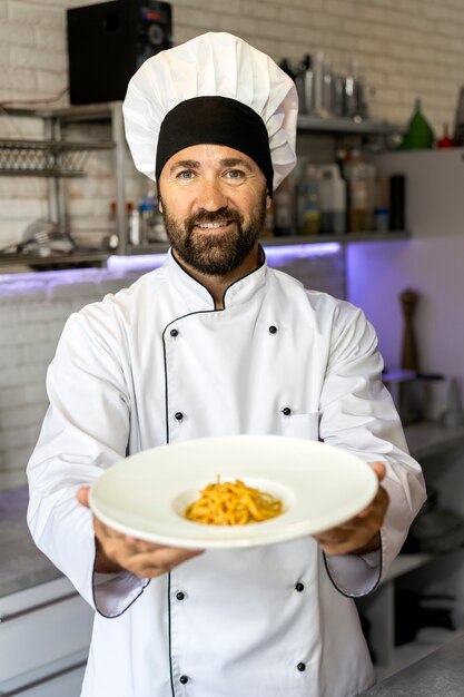 Portret męskiego szefa kuchni w kuchni trzymającego talerz z jedzeniem