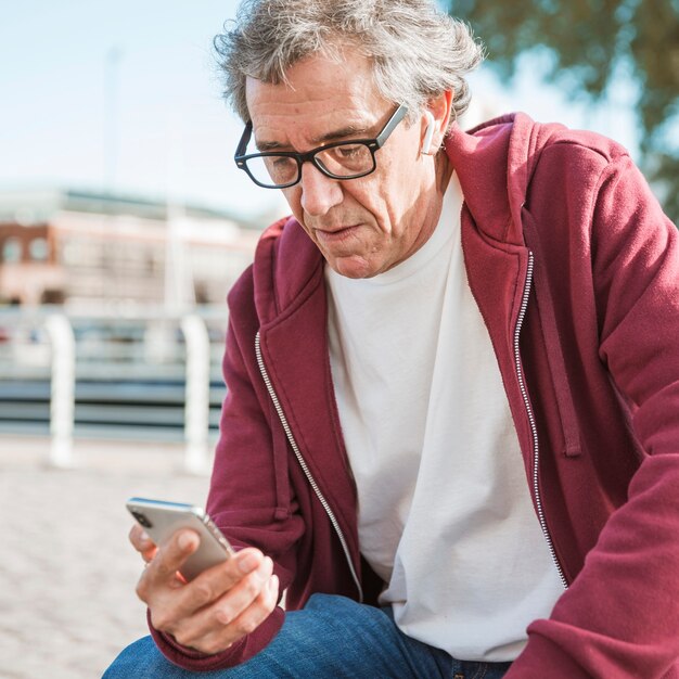 Portret mężczyzna jest ubranym eyeglasses patrzeje smartphone
