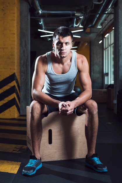 Portret mężczyzna obsiadanie na drewnianym pudełku w gym