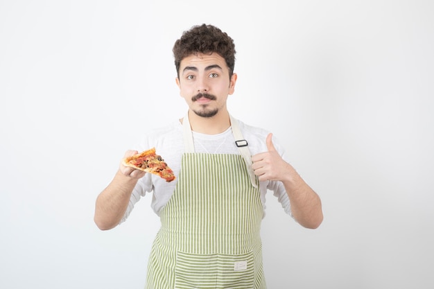 Portret mężczyzny kucharza trzymającego kawałek pizzy i pokazującego kciuk w górę
